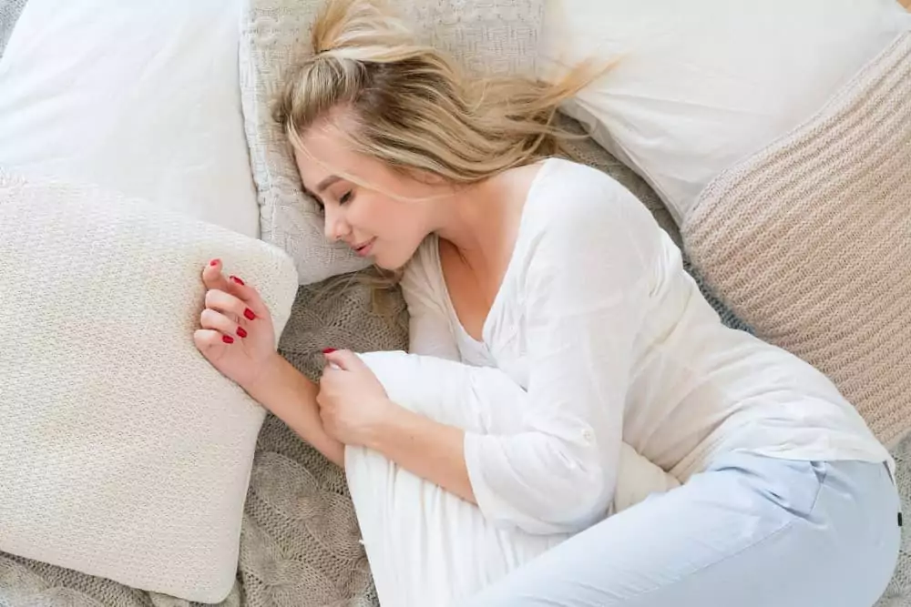 Eine junge blonde Frau schläft friedlich im Bett und umarmt ihr Kissen.