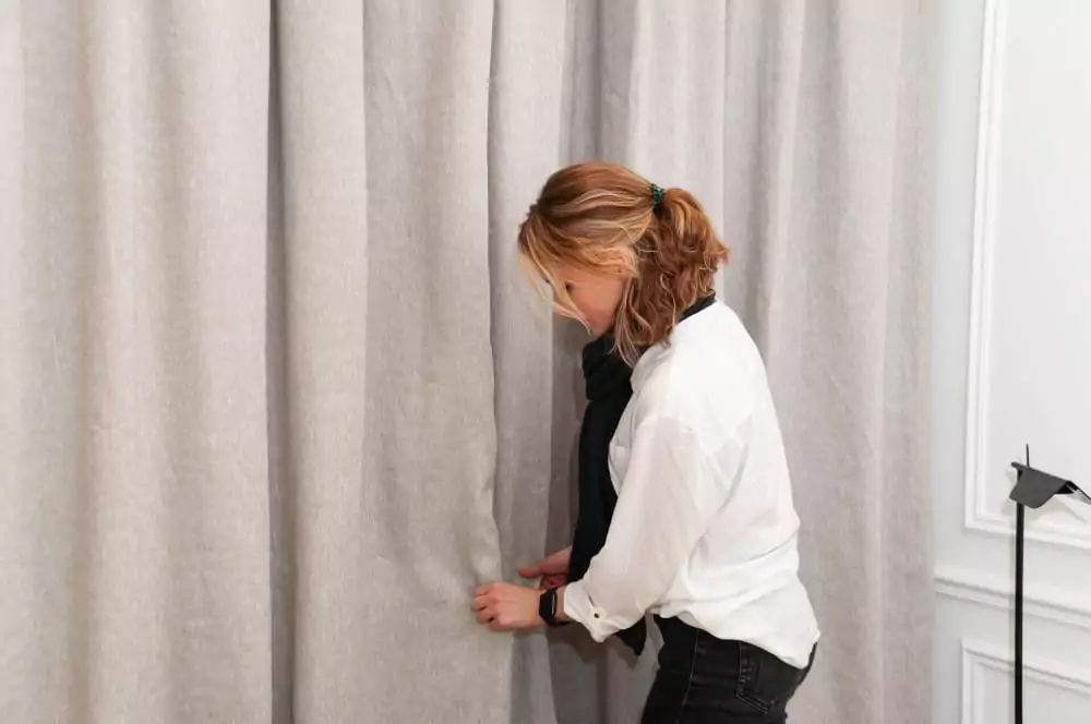 Frau glättet die Falten an den Leinenvorhängen.