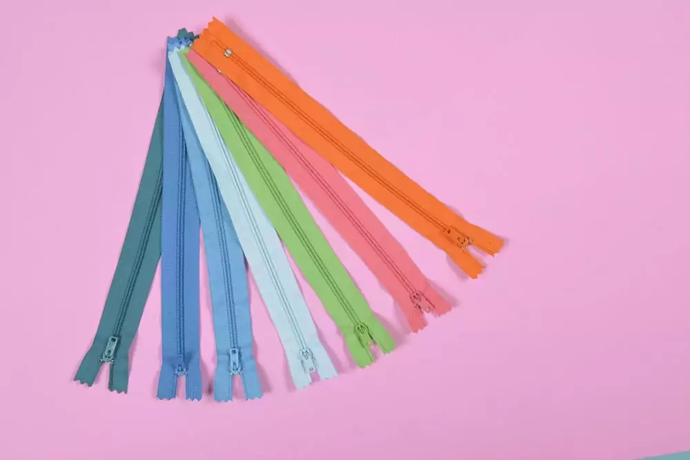 Bunte Reißverschlusse zum Nähen auf rosa Hintergrund, Nähen und Handarbeit Konzept.