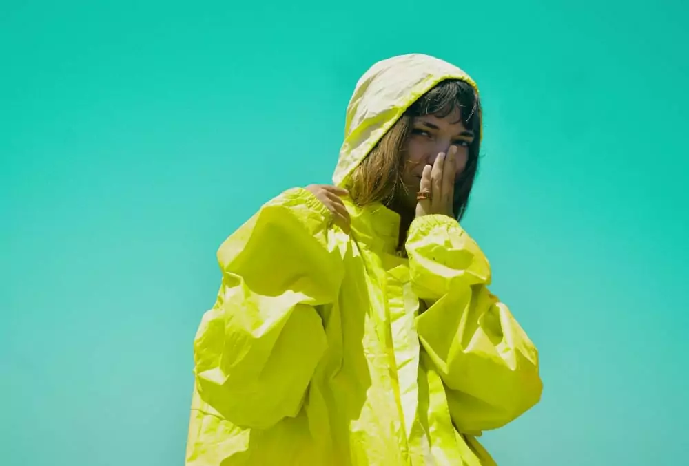 Frau trägt eine leuchtend gelbe Ortalion-Regenjacke vor türkisfarbenem Himmel – Symbolbild für leichten, wetterfesten Outdoorstoff.