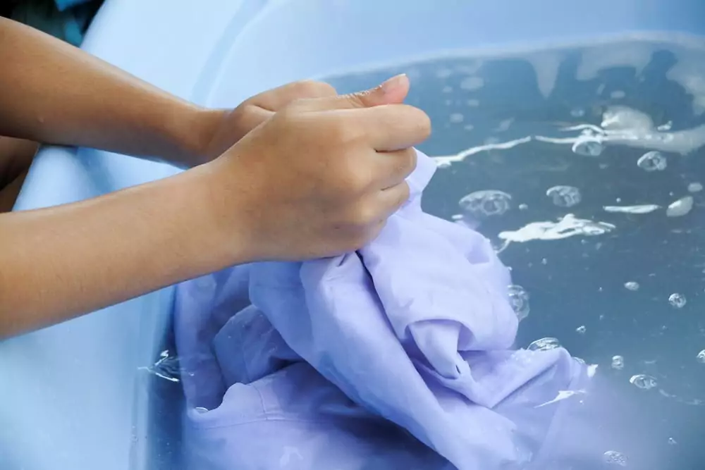 Nahaufnahme von Händen, die Kleidung in einer Wanne waschen