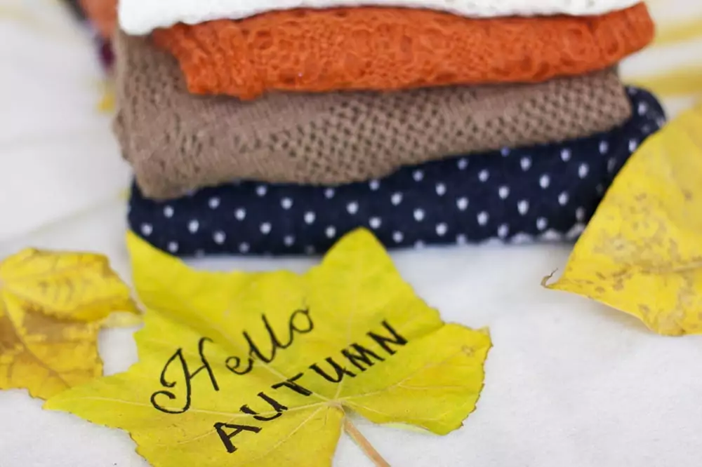 Ein Stapel warmer Pullover und ein gelbes Ahornblatt