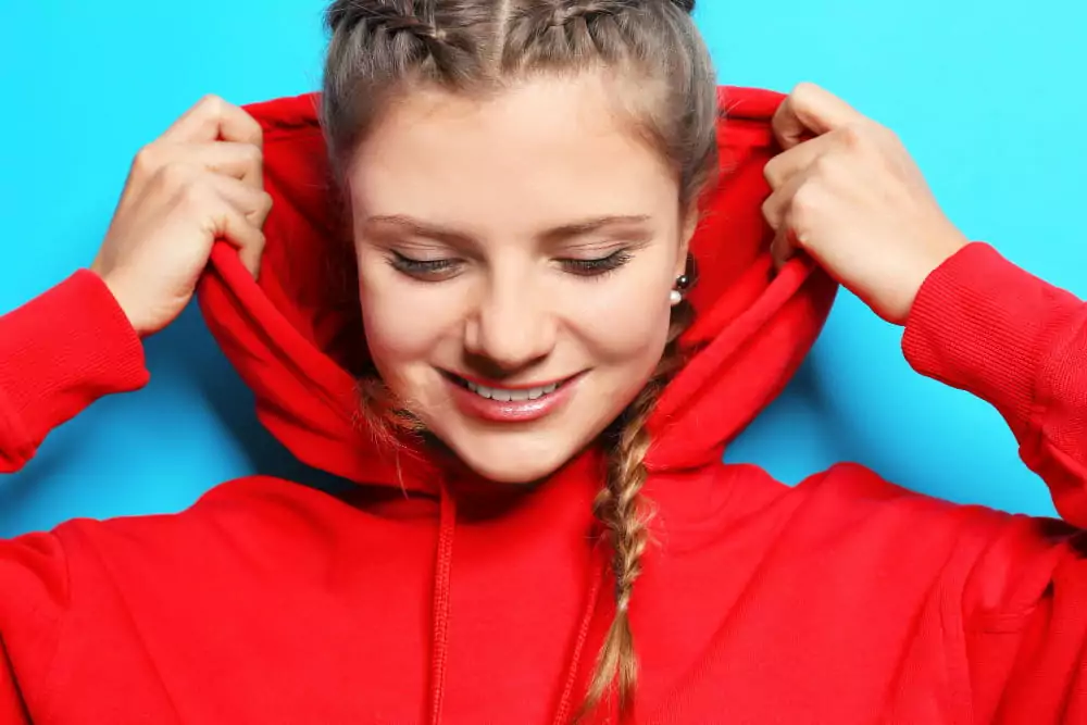 Eine junge, schöne Frau im Hoodie vor farbigem Hintergrund.