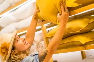 Nahaufnahme einer Frau, die in einem Einrichtungsgeschäft im Einkaufszentrum ein gelbes Kissen aussucht und in die Hand nimmt 