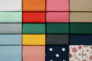 Farbfächer aus 16 verschiedenfarbigen Panama-Stoffen, geordnet in vier Reihen, mit Uni-Tönen wie Mint, Pink, Grau, Blau, Gelb, Dunkelgrün, Navy und Mustern wie Sternen und Rentieren – zeigt die große Auswahl an Dekostoffen
