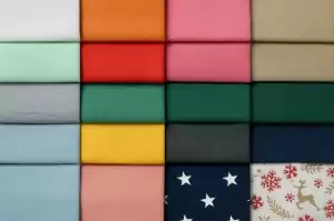 „Farbfächer aus 16 verschiedenfarbigen Panama-Stoffen, geordnet in vier Reihen, mit Uni-Tönen wie Mint, Pink, Grau, Blau, Gelb, Dunkelgrün, Navy und Mustern wie Sternen und Rentieren – zeigt die große Auswahl an Dekostoffen