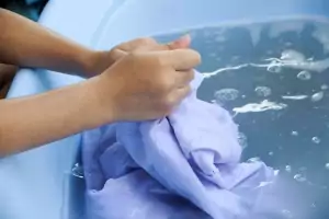 Nahaufnahme von Händen, die Kleidung in einer Wanne waschen