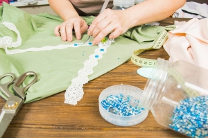 Eine Frau stellt in ihrer Heimwerkstatt Schmuck her. Weibliche Hände, die mit Perlen und Bändern Accessoires herstellen. Schönheit, Kreativität, das Konzept des Handwerks.