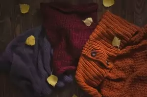 Ein gemütlicher Herbsthintergrund, auf dem warme Strickpullover und Schals auf einem Holzhintergrund zu sehen sind.